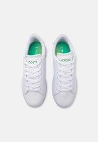Hvite joggesko med glatt lærskinn på oversiden, grønne detaljer på innersålen og snøring; har "Lacoste"-logoen på tungen.