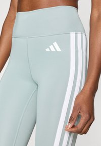 Αθλητικό κολάν ανοιχτού πράσινου χρώματος με ψηλή μέση. Διαθέτει λευκές ρίγες στα πλαϊνά και το λογότυπο της adidas σε λευκό στο μπροστινό μέρος. Ο μαλή υφή.