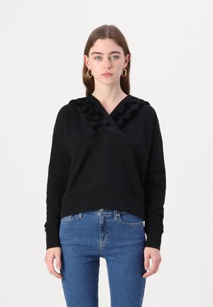 Black sweatshirt with a V-neck design, featuring a textured pattern on the hood. Shown with blue jeans, presenting a relaxed fit.