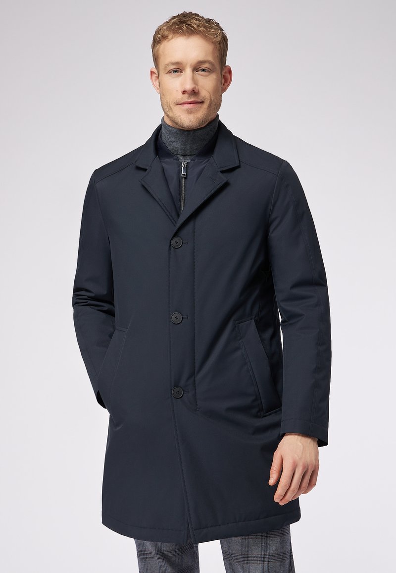 Cappotto blu navy, fino al ginocchio, con colletto a punte, chiusura a quattro bottoni e tasche laterali. Realizzato in tessuto liscio con un design strutturato.