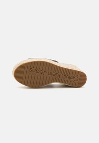Suola di espadriglia con una base in gomma marrone texturizzata, bordata in juta intrecciata beige, con il nome del marchio impresso sul fondo.