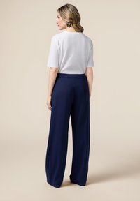 Vit kortärmad topp kombinerad med mörkblå vida byxor. Slät tyg med en ren design. Guldbladsörhängen ger en märkbar accent.