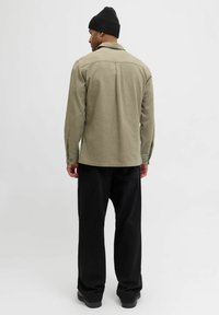 Olivengrønn skjorte med knapper og lange ermer, detaljer på bakstykket, kombinert med svarte vidbukser og svart ribbestrikket lue.