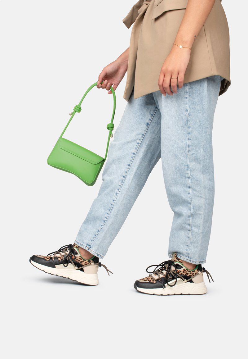 Sneaker mit einem Leopardenmuster-Obermaterial, schwarzen Akzenten und weißer Sohle; hellblaue, lässige Jeans; kleine grüne Handtasche mit Knotengriffen.
