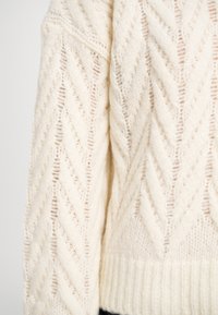 Pull en maille épaisse crème avec un motif en chevrons texturé, doté de poignets et d'un ourlet côtelés, et d'une coupe ample et décontractée.