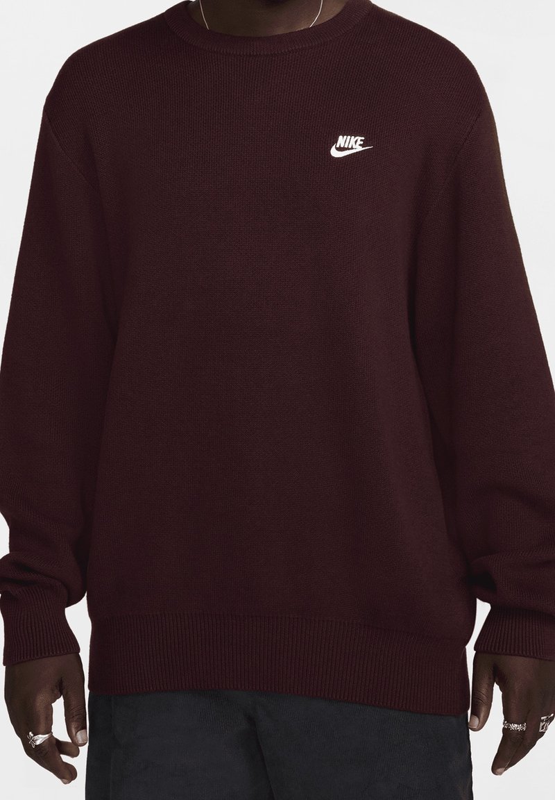 Burgundy stickad tröja med rund halsringning, ribbade ärmslut och nederkant, samt en vit Nike-logotyp broderad på vänster bröst.