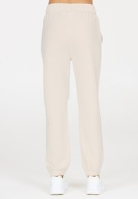Helle beige Jogginghose mit elastischem Bund und elastischen Bündchen, ausgestattet mit zwei seitlichen Taschen und einer glatten, weichen Stofftextur.
