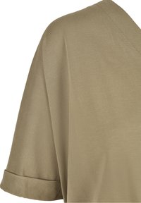 Manche de chemise kaki à manches courtes avec revers retroussé et couture visible sur un tissu lisse.