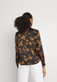 Blusa nera con un motivo floreale in marrone. Presenta maniche lunghe, colletto e una texture liscia. L'orlo è leggermente curvato sul retro.