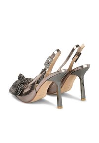 Zapatos de tacón slingback metálicos plateados con un lazo texturizado y acentos de rhinestone. Tacón de aguja único con un detalle de punta cuadrada dorada.