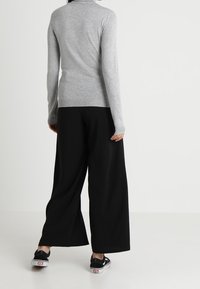 Szary, dopasowany sweter z golfem w zestawie z luźnymi czarnymi spodniami i czarnymi sneakersami. Miękka tekstura; minimalistyczny design.