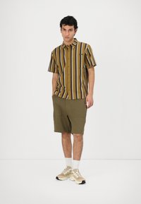 Short-sleeve striped shirt in brown, mustard, and white, paired with olive green shorts. Shoes are beige with light laces and white ankle socks.
