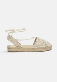 Sandale espadrille tissée en beige, avec une tige texturée, une semelle intermédiaire en jute tressé et des liens à la cheville pour un maintien sécurisé.