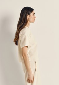 Crèmekleurige top met korte mouwen van een zachte, gestructureerde stof; heeft een ontspannen pasvorm en een ronde halslijn, gecombineerd met bijpassende gestructureerde broek.