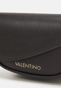 Borsa a pochette in pelle nera con una patta curvata, accento del logo dorato e una texture liscia con sottili dettagli di cucitura.