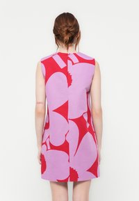 Rochie fără mâneci, cu o bază roz și modele florale mari, roșii. Spatele are o cusătură centrală și o deschidere mică la gât, cu închidere.
