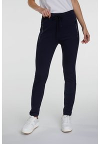 Marina joggers med sidofickor med dragkedja, dragsko i midjan, avsmalnande ben och en strukturerad tyg. Parat med vita sneakers för en aktiv look.