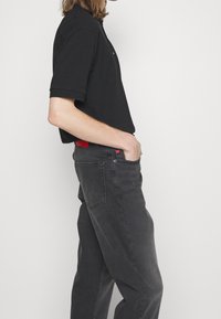 Polo nero e jeans grigio scuro. Il polo ha maniche corte e colletto. I jeans presentano un accento rosso sulla vita e tasche laterali.