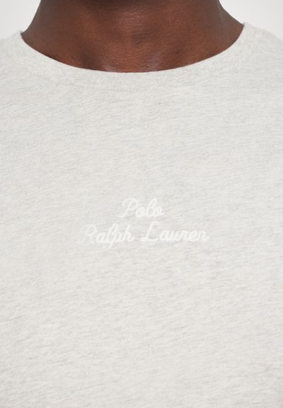 Pilka medvilninė marškinėliai su apvaliu kaklu, priekyje esantis baltas siuvinėtas tekstas "Polo Ralph Lauren", lygus paviršius.