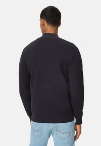Navy ribbet pullover med stående krave og lige kant. Lavet af blødt materiale, med et diskret logo bagpå. Parret med lyse jeans.