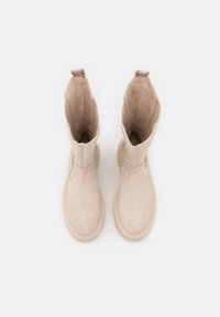 Beige suede ankle boots with a rounded toe, contrasting textured lining, and pull tabs at the cuffs for easy wear.