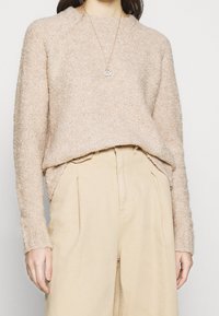 Hellbeige gestrickter Pullover mit einer strukturierten Oberfläche, Rundhalsausschnitt und leicht verkürztem Saum, kombiniert mit beigen weit geschnittenen Hosen.