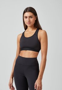 Zwarte sportbeha met brede banden, naadloos ontwerp en een zachte elastische band. Gecombineerd met hoge zwarte leggings voor een strakke uitstraling.