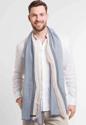 Lightweight scarf in blue, grey, and beige stripes. Frayed edges with a soft texture; worn draped around the neck over a white shirt.