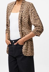 Blazer à imprimé léopard avec devant ouvert, manches trois-quarts, en tissu doux ; porté sur un haut blanc et un pantalon noir.