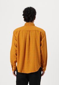 Camicia a maniche lunghe a quadretti in vivaci tonalità di arancione e giallo. Presenta un colletto con bottoni e bottoni ai polsini, con una vestibilità rilassata e una piega sul retro.
