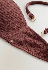 Barna texturált szövet bikini felső levehető pántokkal és aranyszínű fém kiegészítőkkel, fehér felületen.