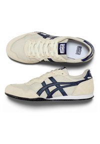Chaussures de course Onitsuka Tiger beige et bleu marine avec accents en daim, lacets et bandes latérales signature, vues de dessus et de côté.