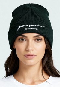 Bonnet en tricot côtelé vert foncé avec texte brodé en blanc « suis ton cœur » et design de flèche, coupe ajustée, texture lisse.