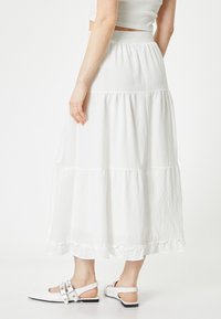 Falda larga blanca de capas con un dobladillo con volantes, fabricada en tejido ligero. Combinada con zapatos blancos de punta abierta con un diseño de tira.