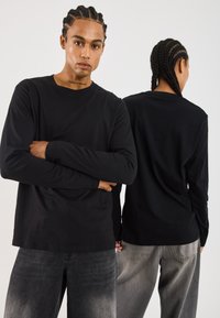 Schwarzes Langarm-T-Shirt aus einem glatten Stoff, mit Rundhalsausschnitt und lockerer Passform, kombiniert mit verwaschenen grauen Jeans.