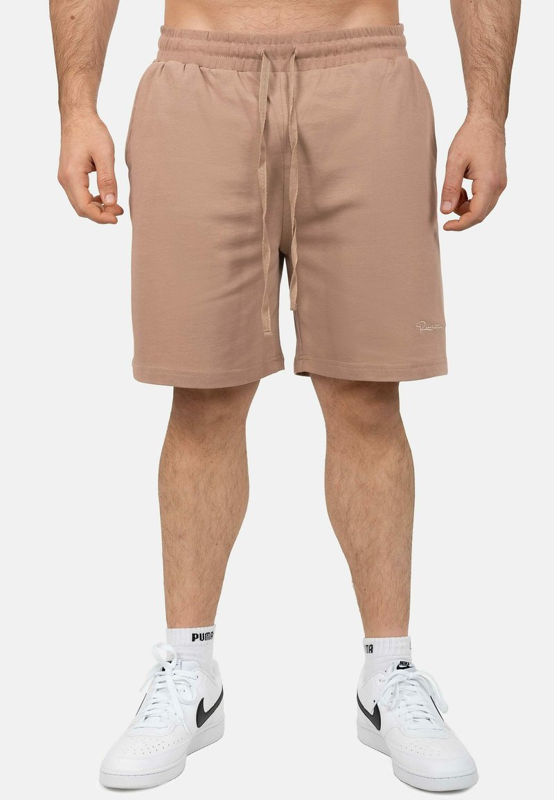 Pantaloni sportivi di colore marrone chiaro con cintura elastica e cordoncino. Tessuto morbido, tasche laterali e dettaglio del logo sulla gamba.