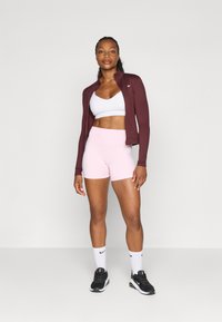 Bordeaux zipzáras dzseki, fehér sportmelltartó, rózsaszín, magas derekú rövidnadrág, fekete sportcipő és fehér zokni fekete logókkal. Sima anyag, testhezálló fazon.