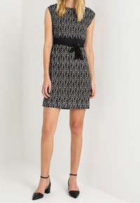 Czarna i biała sukienka w wzory z krótkimi rękawami, zwężona w talii z kokardą, w połączeniu z czarnymi płaskimi butami na szpic.