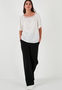 White blouse with lace detailing around the square neckline, short puff sleeves, paired with loose black trousers and white sneakers.
