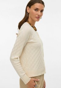Kremowy kardigan w teksturowany wzór diamentowy, z prążkowanymi mankietami i zapięciem na guziki. Miękki, lekki materiał o dopasowanym kroju.
