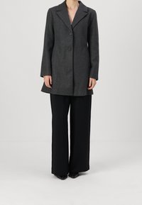 Grå ullblandad kappa med klädd krage, två knappar och långa ärmar; kombinerad med svarta vida byxor.