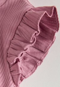 Roza rebrasta tkanina z volanastim robom. Tekstura je mehka z rahlim raztezanjem, z valovitim robom na spodnjem delu in natančnim šivanjem.