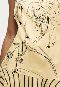 Κίτρινο τοπ με μεγάλα μαύρα σχέδια λουλουδιών συνδυασμένο με κίτρινη φούστα με κάθετες μαύρες ρίγες, φορεμένα από ένα άτομο με καφέ επιδερμίδα.