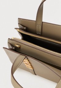 Khaki kabelka se zlatými kovovými doplňky, dvěma odděleními a zapínáním na zip. Má strukturovaný povrch a krátká madla pro snadné nošení.