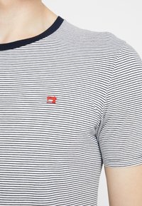 Gestreept T-shirt in marineblauw en wit, met korte mouwen en een rood logo. Klassieke ronde halslijn met een contrasterende marineblauwe afwerking. Katoenen materiaal.