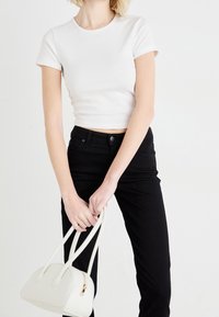 Valkoinen lyhyt t-paita, jossa on lyhyet hihat, yhdistetty mustiin istuviin housuihin. Pitelee pientä valkoista käsilaukkua, joka on rakenteellisesti muotoiltu ja siinä on tuplakahvat.