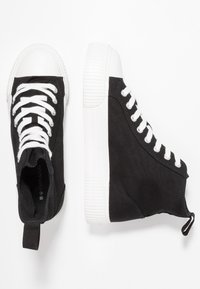 Sorte høje sneakers i lærred med hvide gummisåler og snørebånd, der har en trække-flap bagpå og en tekstureret overflade.