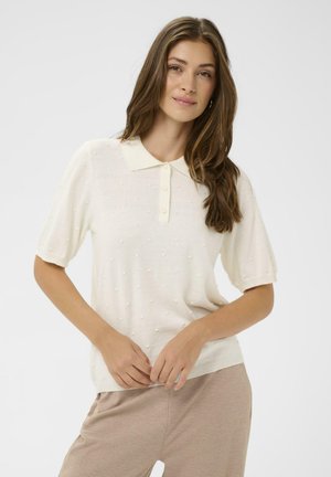 Krém színű rövid ujjú poló pulóver texturált mintával és gombos gallérral, finom kiemelkedő pöttyökkel a részletek kiemelésére.