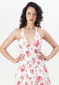 Floral halter neck dress in white with red and gray rose patterns; smocked bodice with ruffled tiers at the hem. Smooth fabric texture.