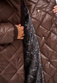 Brązowa pikowana kurtka z jedwabną podszewką w wzór paisley w odcieniach granatu, bieli i pomarańczu. Zapięcie na napy.
